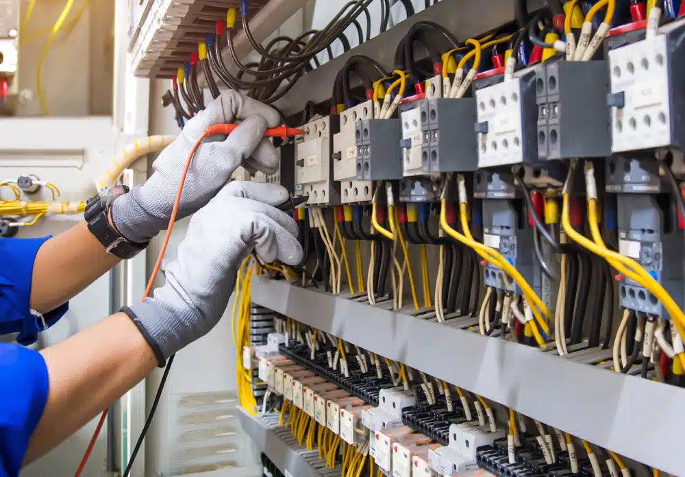 Electrician in work gloves wiring contactors inside a commercial control panel